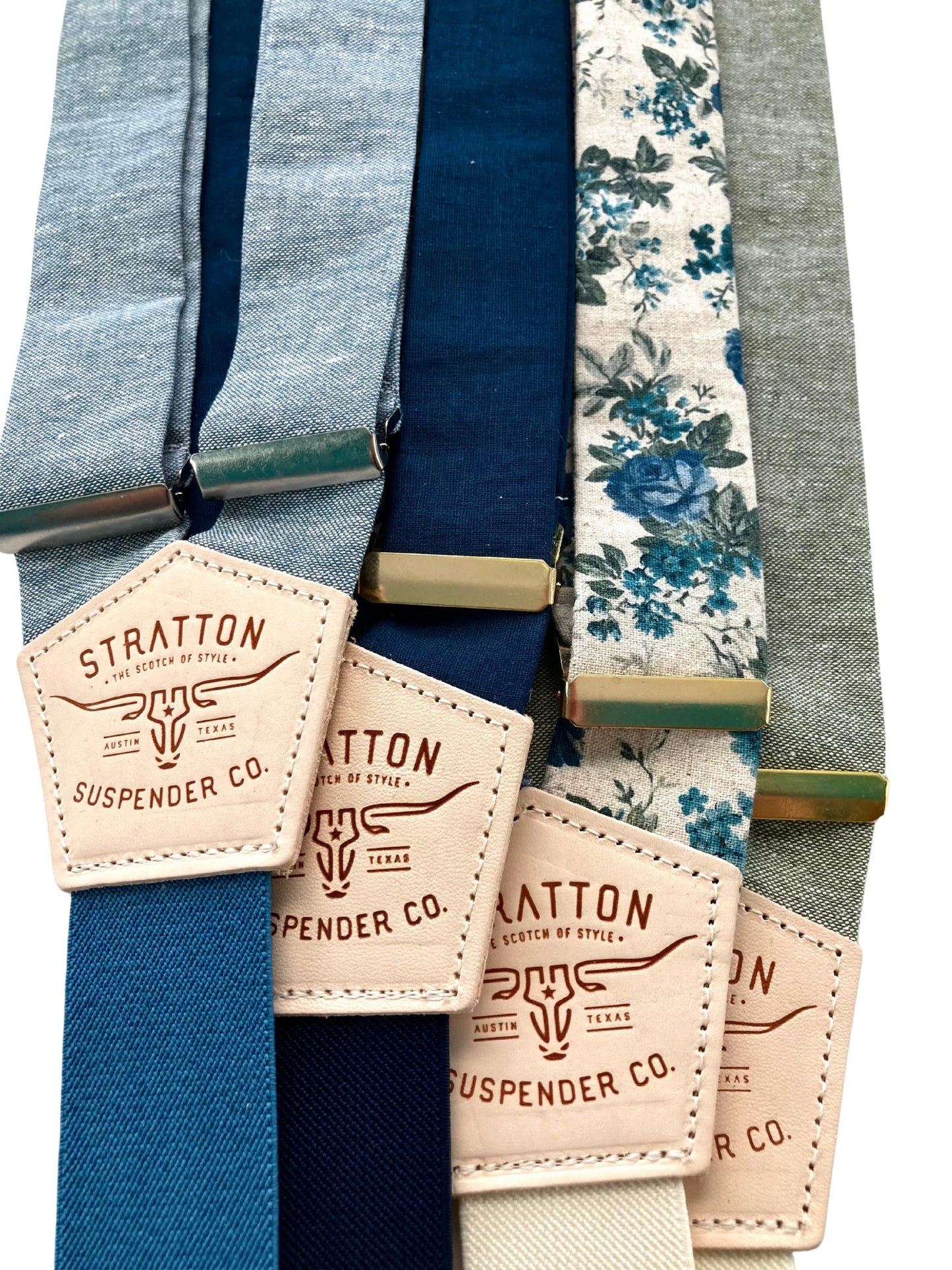 Flat lay of linen suspenders in sky blue, navy, deep blue, floral teal, and sage green with gold and silver adjusters—handmade by Stratton Suspender Co. for weddings, groomsmen, and vintage menswear styling.