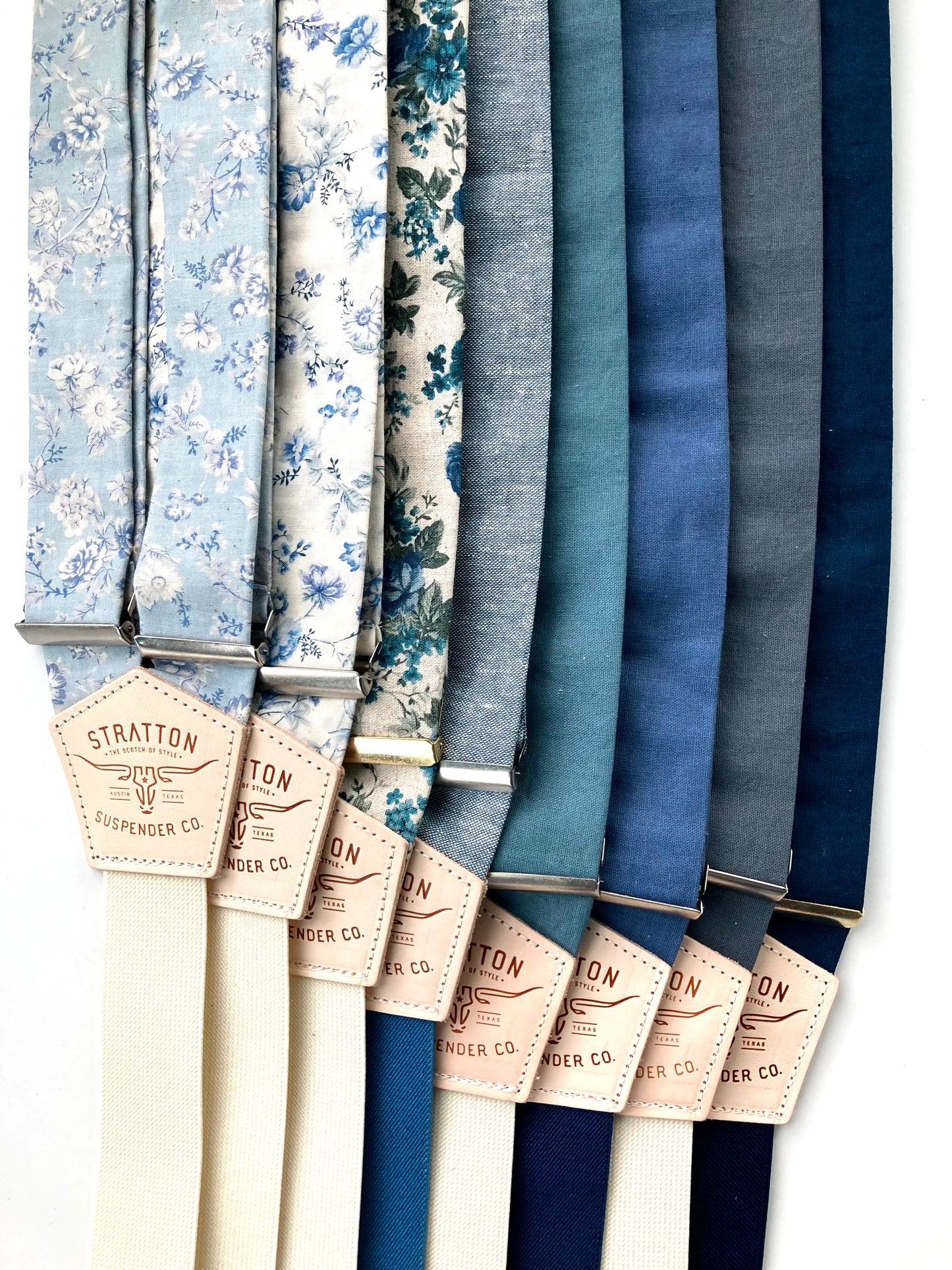 Flat lay of handmade linen suspenders in pale blue, light blue floral, teal, dusty navy, and deep blue—Stratton Suspender Co.’s vintage-inspired collection for weddings and classic menswear.