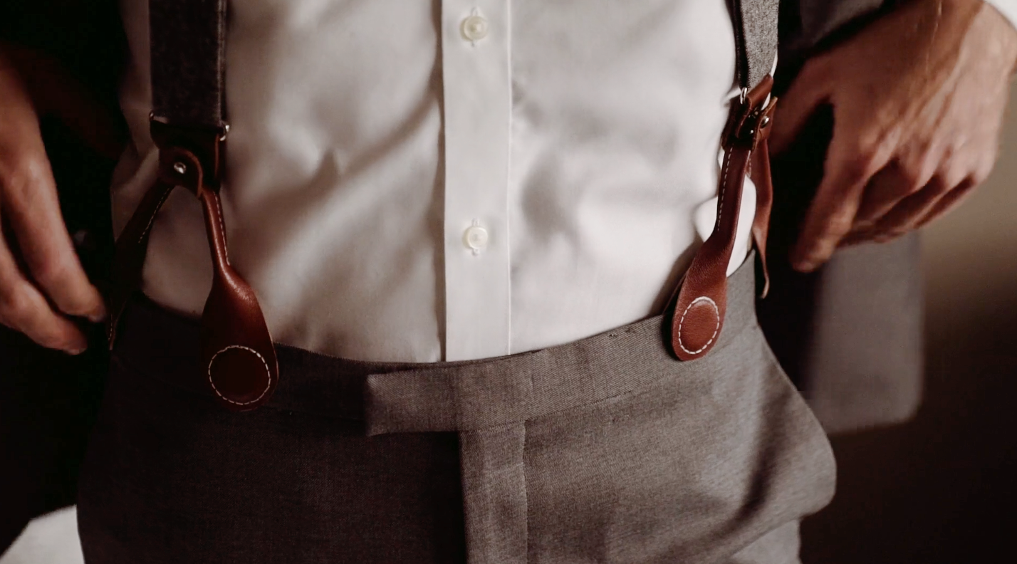 Close-up of magnetic clasp suspenders worn with a formal suit. Rich brown leather loops securely attach to waistband, offering a refined alternative to clip-ons. Perfect for weddings and formal menswear.