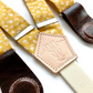 Close-up of marigold floral cotton suspenders with chocolate leather magnetic clasps, vintage-inspired accessory.