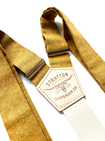 Close-up of marigold yellow rustic wedding suspenders with cream elastic back strap, brushed metal adjusters, and Stratton leather logo patch.