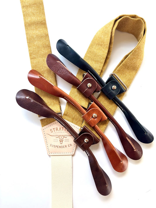 Close-up of rustic marigold suspenders with interchangeable leather tabs in black and brown tones—perfect for custom groomsmen wedding orders.