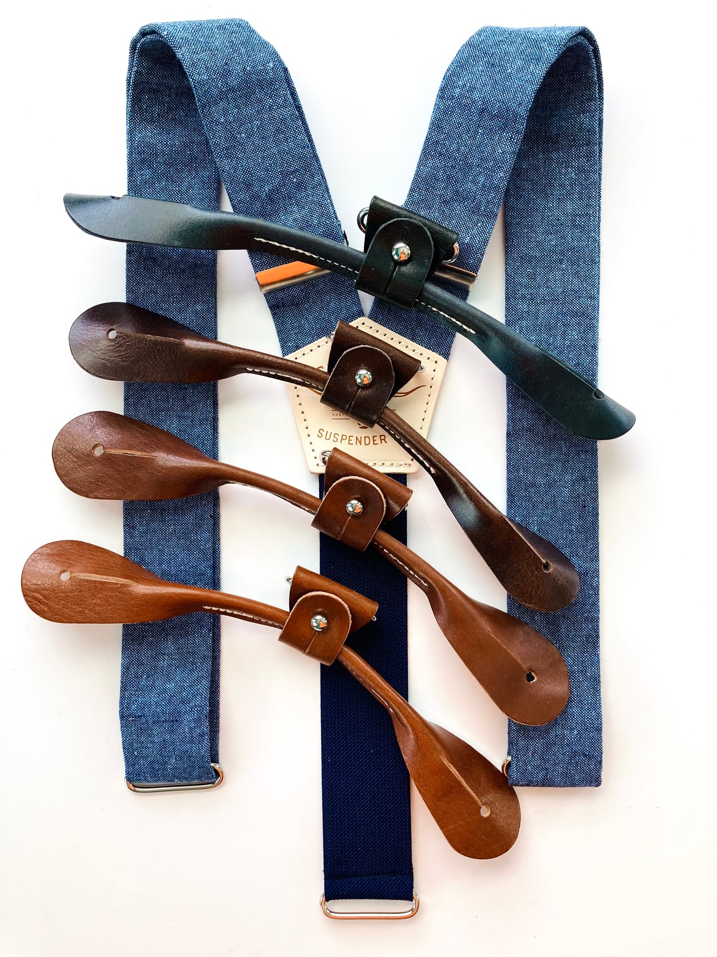 Stratton Suspender Co. Nautical Blue linen suspenders with navy elastic back and four full-grain leather button-on tab color options—black, dark brown, chestnut, and saddle tan—displayed on a white background.