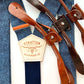 Close-up of Stratton Suspender Co. Nautical Blue linen suspenders featuring the branded leather patch, navy elastic back, and full-grain leather button-on tab options in saddle tan, chestnut, and dark brown.