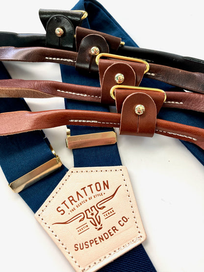Suspenders for men’s formalwear in navy and midnight with customizable leather strap options in neutral tones with gold colored polished brass.