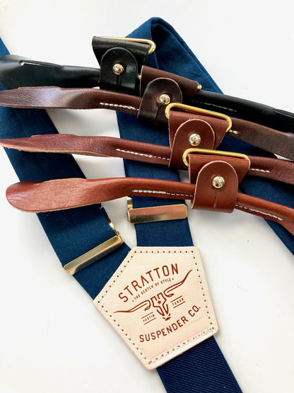 Navy suspenders with gold adjusters and button-on leather ends in black, chocolate, chestnut, and tan, styled for groomsmen or formalwear.