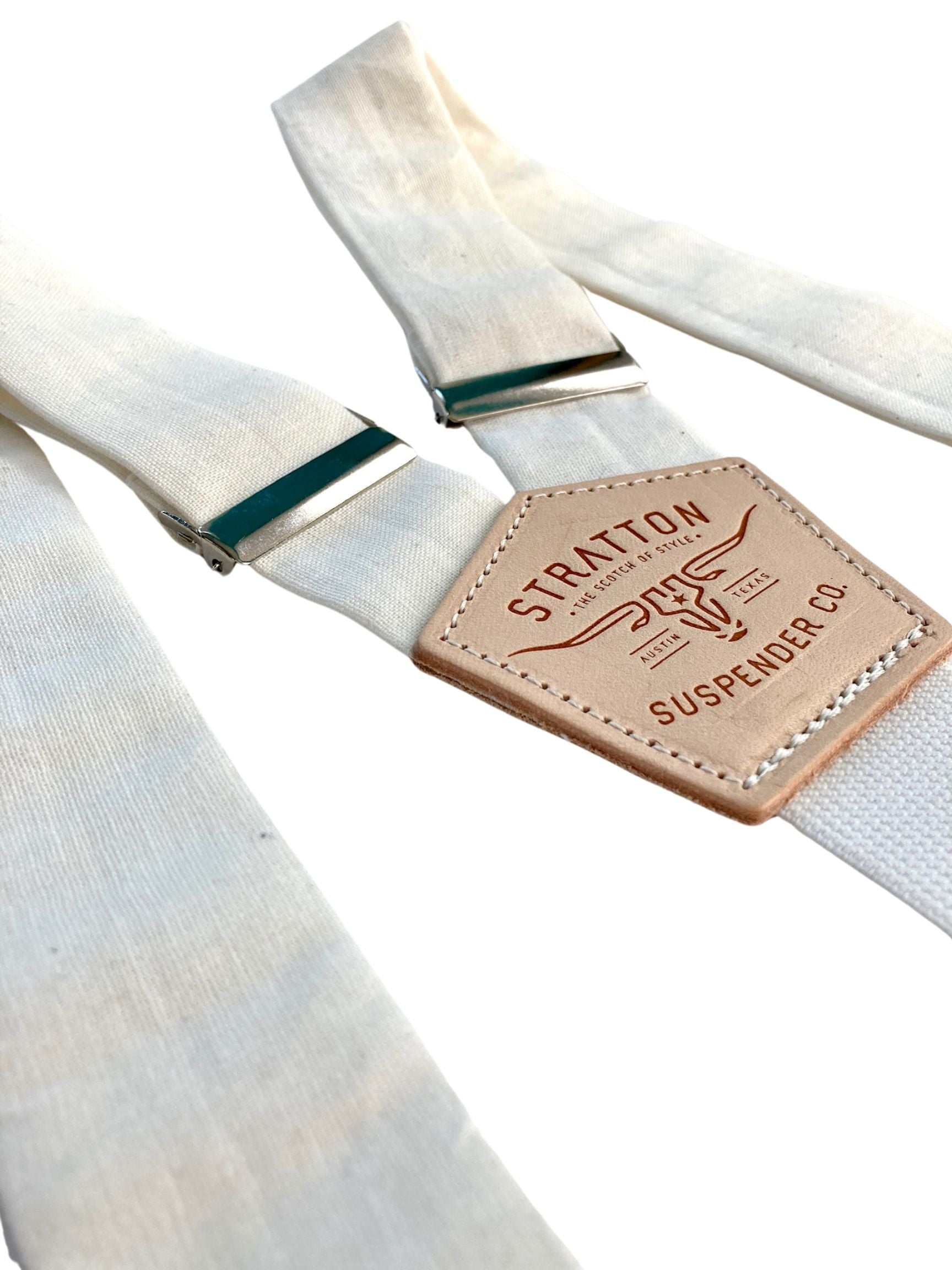 Close-up of pearl white linen suspenders with polished silver adjusters and tan leather back patch, handmade by Stratton Suspender Co for weddings and formalwear.