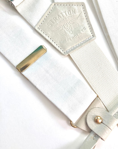 Close-up of pearl white linen suspenders with polished gold adjusters and leather button attachments, handcrafted for weddings, groomsmen, and formal menswear.