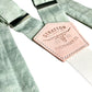 Close-up of pistachio green linen suspenders with natural leather back patch and silver hardware. Handmade in Texas, ideal for rustic weddings, groomsmen, and spring formalwear.