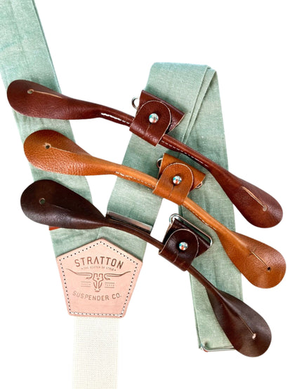 Pistachio green linen button-on suspenders with natural leather detailing, handmade in Texas. Shown with chocolate, saddle, and chestnut leather attachment options. Ideal for groomsmen, summer weddings, and garden ceremonies.