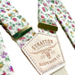 Detailed close-up of Stratton Suspender Co. rose garden floral suspenders with vintage brass adjusters and signature leather patch—handmade wedding braces for grooms and groomsmen, rustic menswear accessory.