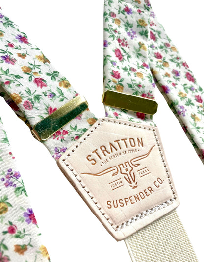 Detailed close-up of Stratton Suspender Co. rose garden floral suspenders with vintage brass adjusters and signature leather patch—handmade wedding braces for grooms and groomsmen, rustic menswear accessory.