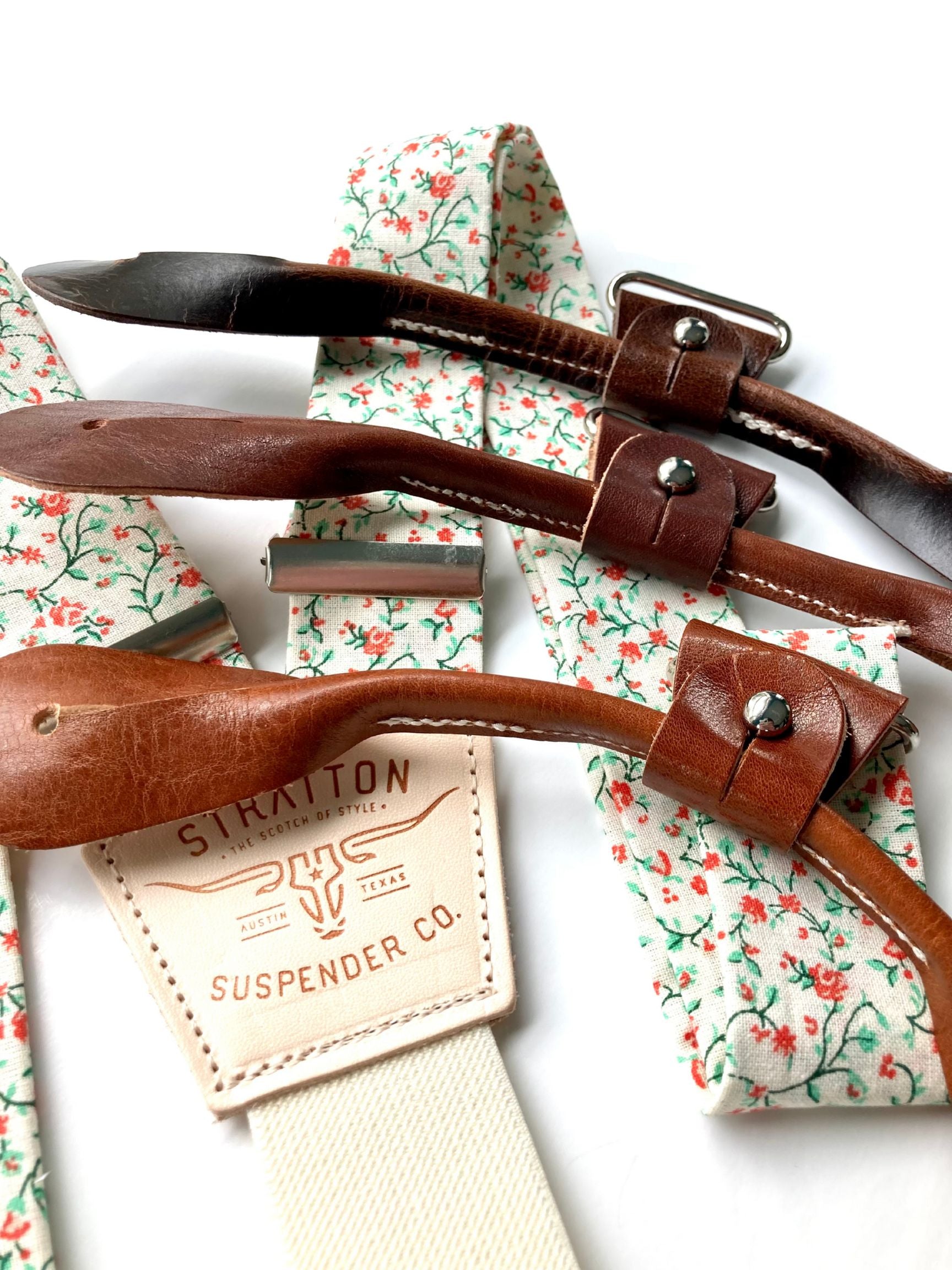 Close-up of rustic orange and green floral suspenders with brown leather button-on loops and cream elastic back, handmade by Stratton Suspender Co. for groomsmen and rustic wedding attire.
