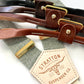 Sage green linen wedding suspenders with ivory elastic back strap, gold adjusters, and four leather button-on options in black, chocolate, cognac, and tan.