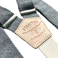 Close-up of Stratton Suspender Co. shale blue linen suspenders with silver adjusters and natural leather back patch, handmade in Texas—classic button-on braces for wedding and formal menswear.