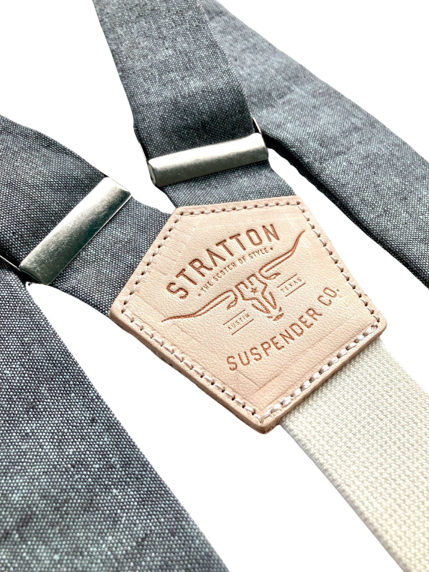 Close-up of Stratton Suspender Co. shale blue linen suspenders with silver adjusters and natural leather back patch, handmade in Texas—classic button-on braces for wedding and formal menswear.