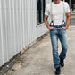 Man walking outdoors wearing silver linen suspenders with black leather button-on loops, styled with a white t-shirt, light wash jeans, and black boots. Rugged menswear look featuring Stratton Suspender Co. handmade suspenders.