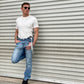 Man wearing a vintage-inspired 1940s heavyweight white t-shirt and wool suspenders by Stratton Suspender Co. Styled with classic denim and black boots, showcasing timeless American workwear against an industrial metal backdrop.