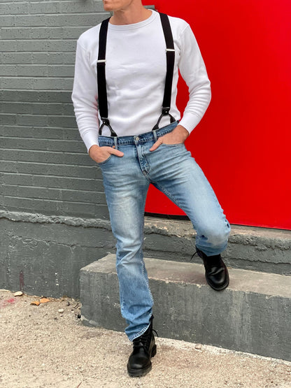 Man wearing a vintage-inspired white waffle knit thermal shirt paired with black suspenders, light-wash vintage Levi’s jeans, and black Dr. Martens boots. Ethically made in the USA, this heavyweight thermal is designed for warmth, durability, and classic American workwear style. Stratton Suspender Co.
