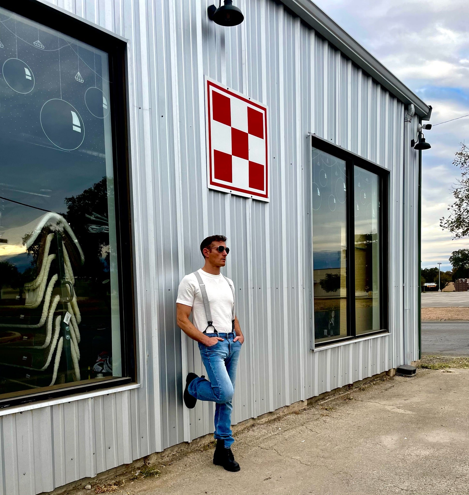 Man wearing gray vintage button-on suspenders with jeans and a t-shirt, leaning against a corrugated metal building. Handmade in Texas, USA – rugged, timeless style.