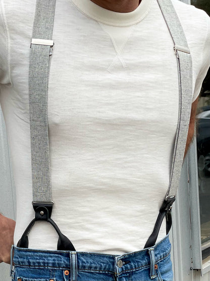 Close-up of vintage charcoal beige linen suspenders with black leather button-on attachments and silver adjusters, styled with jeans and a cream crewneck—ideal for groomsmen, rustic weddings, and modern vintage menswear.