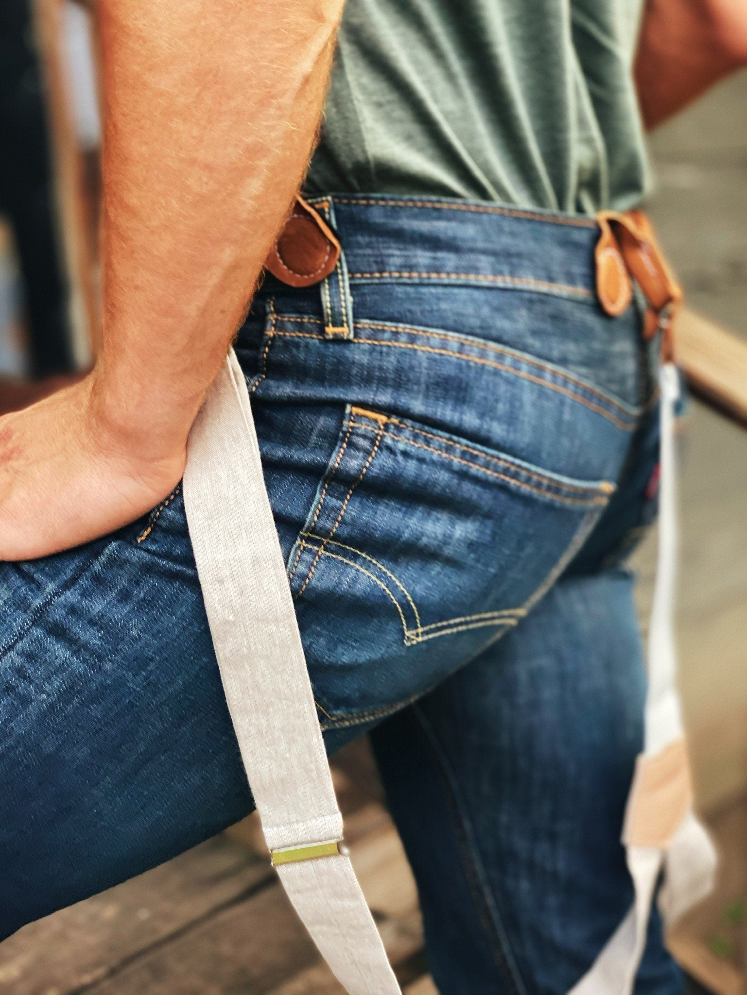 Close-up of vintage ivory beige linen suspenders paired with classic Levi’s denim. Off-the-shoulder style showcasing premium woven fabric and leather button attachments for a timeless, heritage American menswear look.