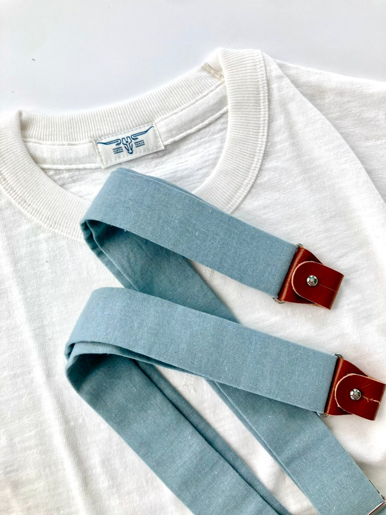 Vintage Pre-War White T-Shirt by Stratton Suspender Co. with Dusty Blue Suspenders featuring brown leather button tabs. Heritage American menswear crafted for timeless style and durability. Ethically made and designed for workwear and classic fashion enthusiasts.