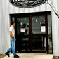 Man wearing handmade vintage suspenders, a white tee, and jeans walking toward the entrance of the Texas Farm Store—showcasing Stratton Suspender Co.’s modern take on classic menswear style, made in Austin, Texas.