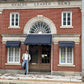 Man wearing a Vintage White Henley and brown wool suspenders by Stratton Suspender Co., standing in front of a historic brick building. Showcasing heritage American workwear, rugged craftsmanship, and timeless menswear style.