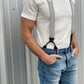 Man wearing a vintage-inspired 1940s heavyweight white t-shirt and gray linen suspenders by Stratton Suspender Co. Styled with classic denim, this rugged yet refined look captures heritage American workwear against an industrial metal wall.