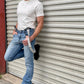 Man wearing a vintage-inspired 1940s heavyweight white t-shirt with gray linen suspenders by Stratton Suspender Co. Styled with classic denim and rugged black boots, this heritage menswear look is captured against an industrial metal backdrop, embodying timeless American workwear.