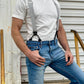Close-up of a man wearing a vintage 1940s heavyweight white t-shirt and gray linen suspenders by Stratton Suspender Co. Paired with classic blue jeans, the rugged industrial setting highlights the timeless appeal of heritage American workwear and handcrafted menswear.