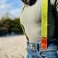 Close-up of women’s chartreuse green linen suspenders with tan magnetic clasps styled with high-rise denim.