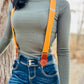 Women’s tangerine orange linen suspenders with tan leather magnetic clasps styled with high-rise denim jeans and fitted long-sleeve top.