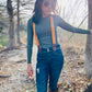 Women’s tangerine orange linen suspenders with tan magnetic clasps styled with high-rise jeans, boots, and fitted top in a rustic fall outdoor setting.