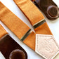 Detail of women’s tangerine orange linen suspenders with chocolate leather magnetic clasps on white background.