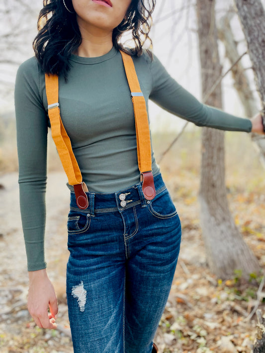 Women’s tangerine orange linen suspenders with tan magnetic clasps styled with distressed denim and ribbed top in a fall outdoor setting.