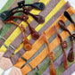 Stratton Suspender Co. Fall Linen Collection straps laid out in the following order: Spruce (bright green), Nutmeg (brown), Yellow, Maroon (rust), Orange, Olive Green, Palm Green (green and yellow woven linen), Purple with both magnetic and button-on attachments laid out on top in the following order: Black, Chocolate (dark brown), Cognac (reddish brown), Tan (light brown)