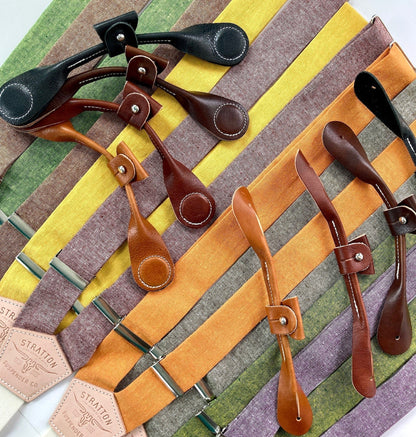 Stratton Suspender Co. Fall Linen Collection straps laid out in the following order: Spruce (bright green), Nutmeg (brown), Yellow, Maroon (rust), Orange, Olive Green, Palm Green (green and yellow woven linen), Purple with both magnetic and button-on attachments laid out on top in the following order: Black, Chocolate (dark brown), Cognac (reddish brown), Tan (light brown)
