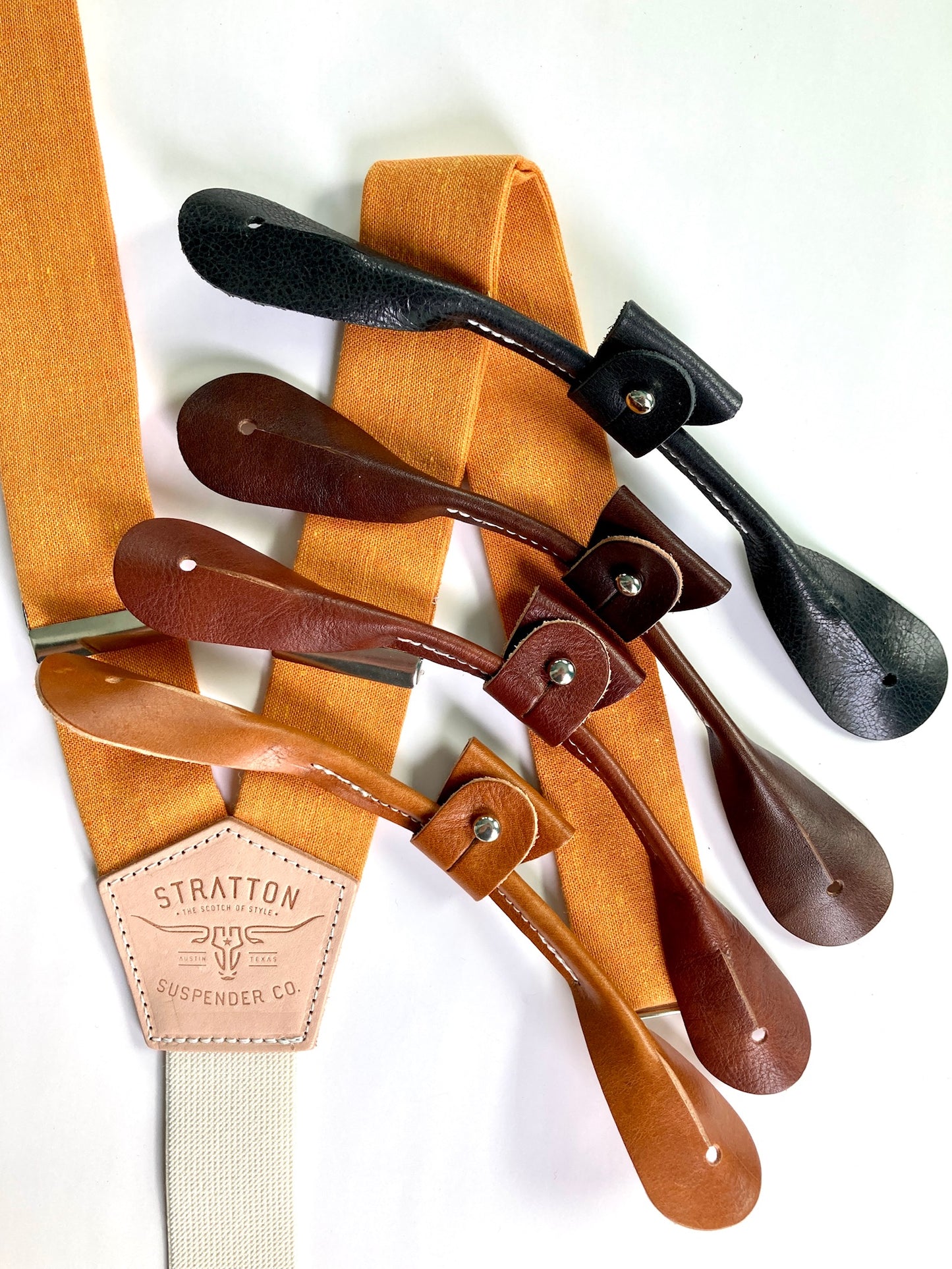 Orange Linen Stratton Suspender Co. Set with one button on attachment in the following colors from top to bottom: Black, Chocolate (dark brown), Cognac (reddish brown), Tan (light brown)