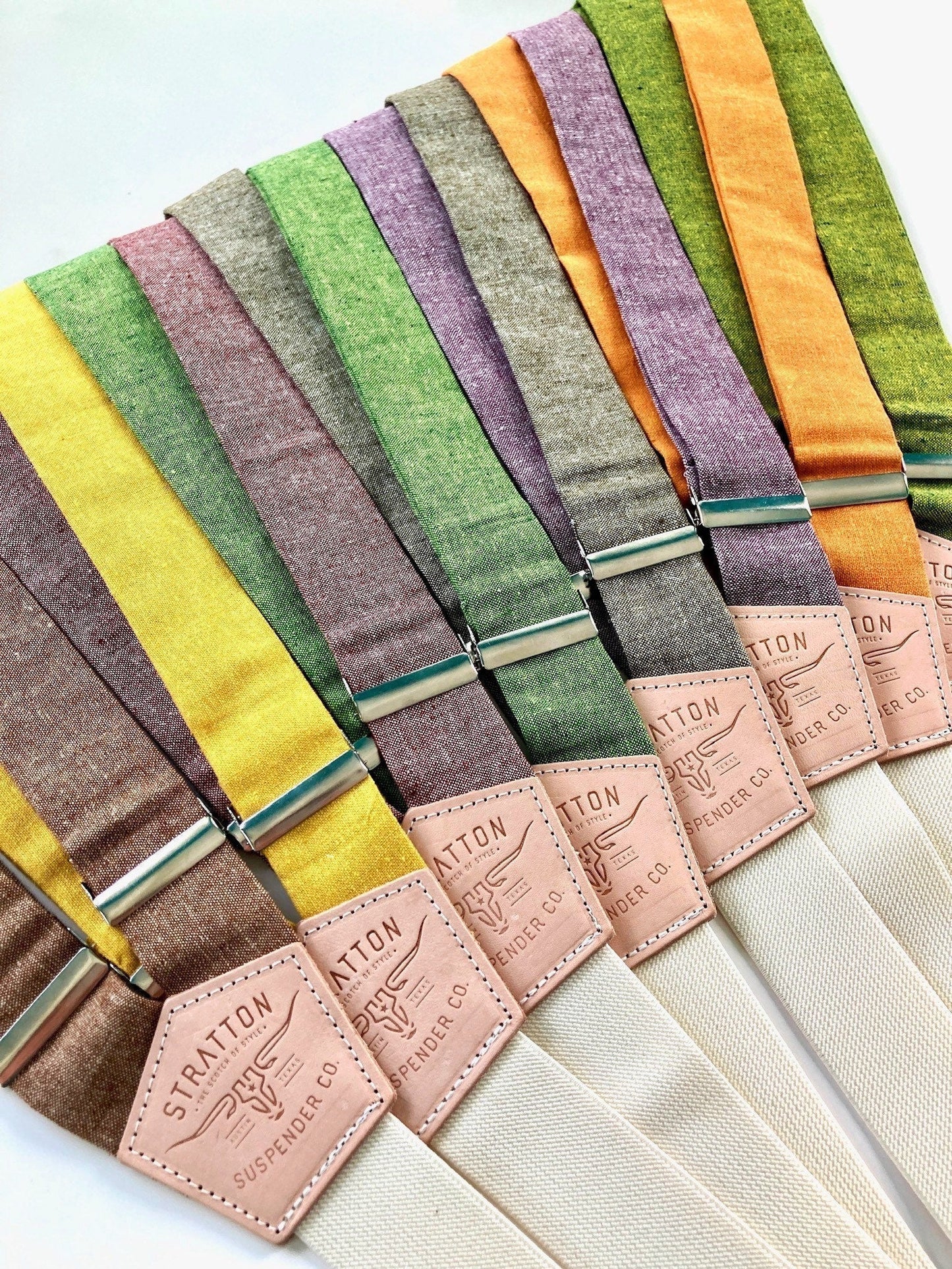 Stratton Suspender Co. Fall Linen Collection laid out in the following order: Nutmeg (Brown), Yellow, Maroon or Rust, Spruce (Bright Green), Olive Green, Purple, Orange, Palm (green and yellow woven linen)